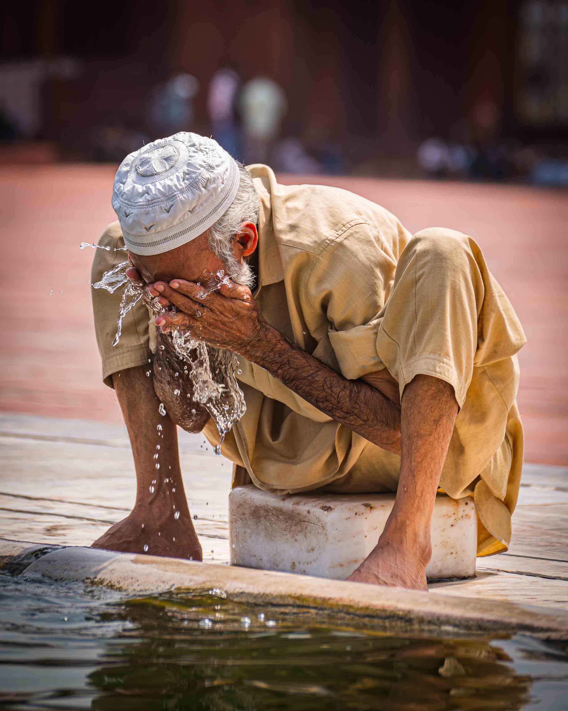 Elderly man in a prayer cap washing his face at the ablution fountain of the Jama Masjid mosque, Old Delhi, India
