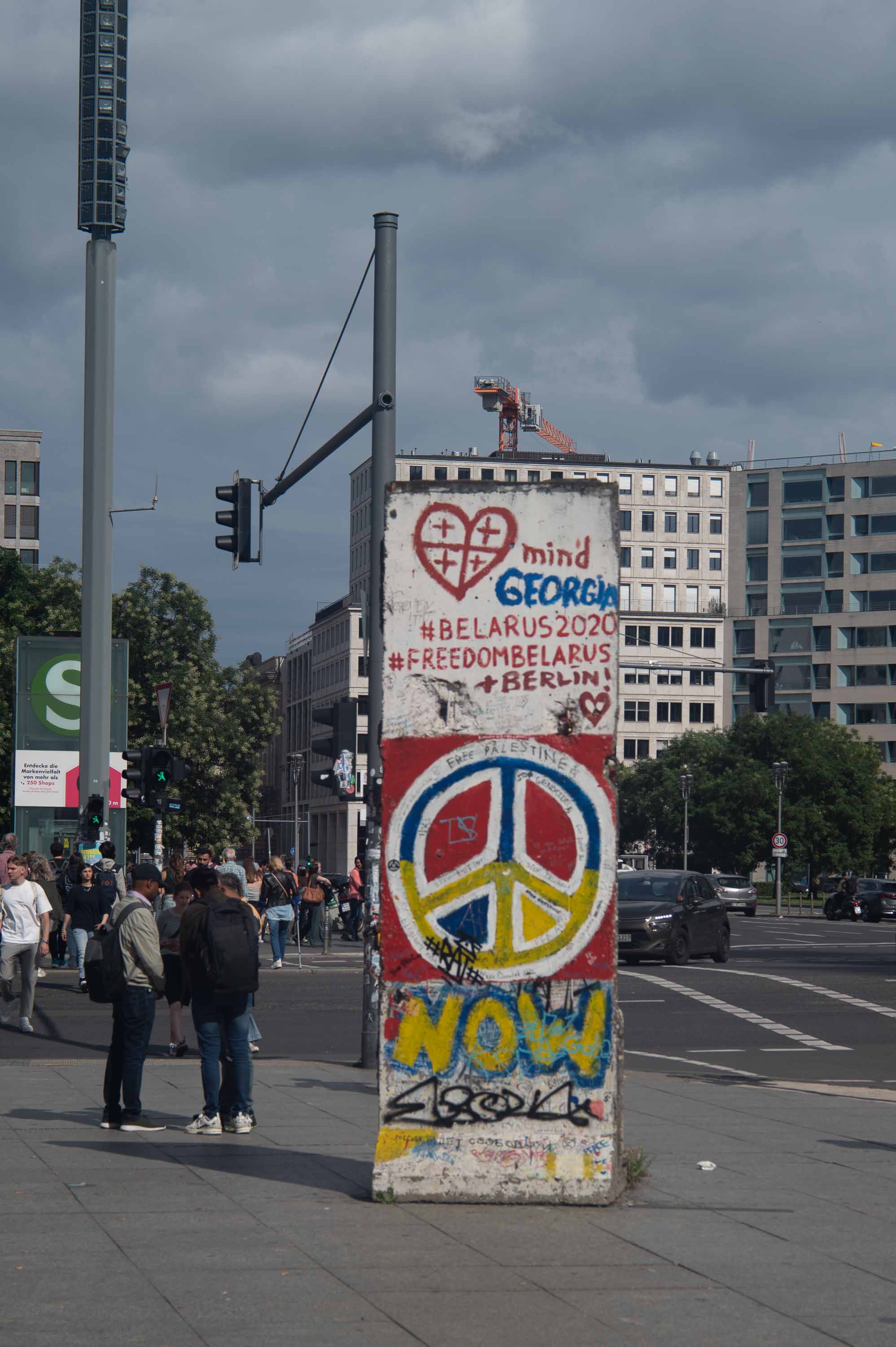A fragment of the Wall, covered in graffiti and present-day slogans, standing in the middle of a square.