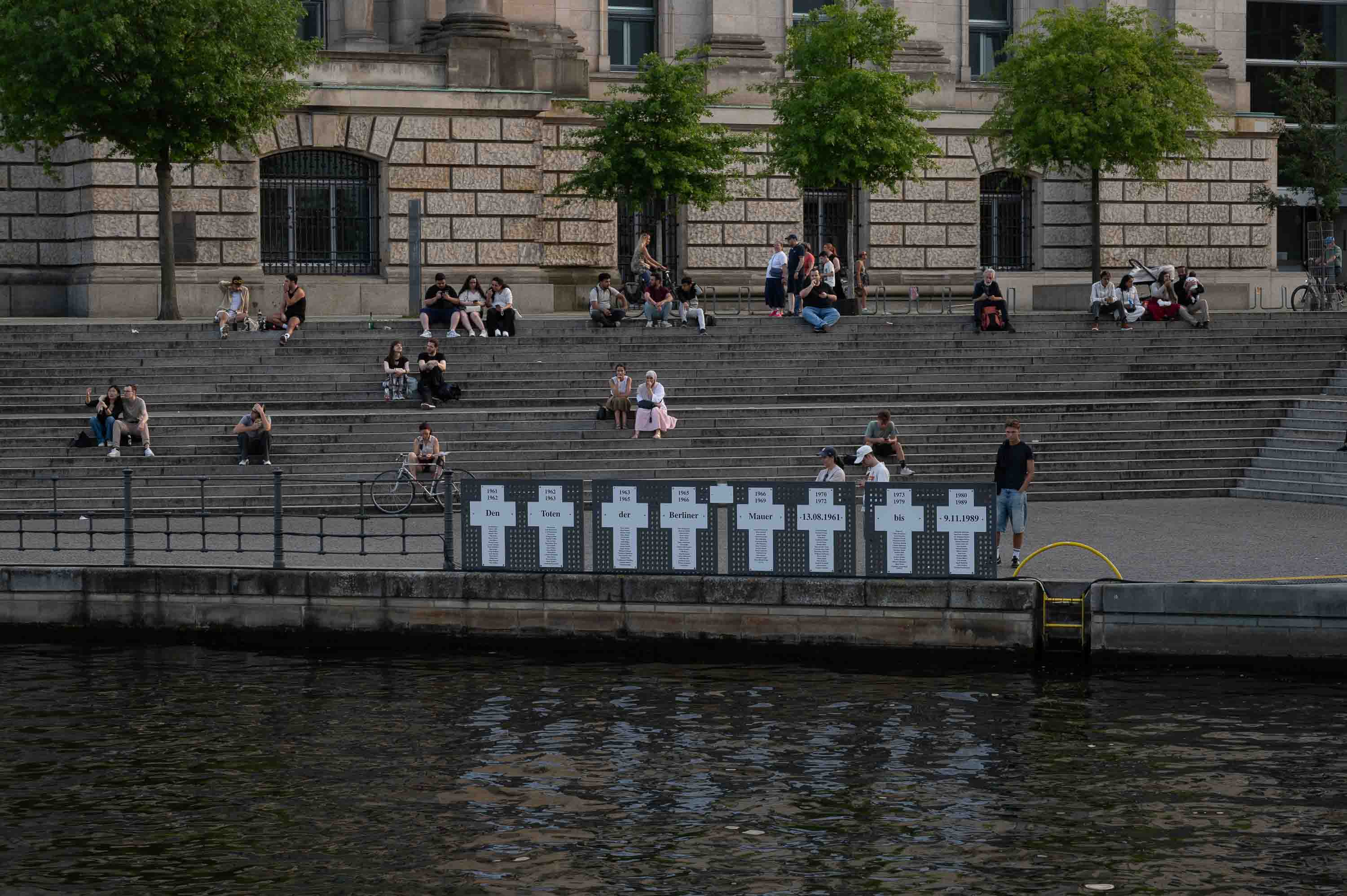 A memorial to those who died at the Wall, on the banks of the Spree, while life goes on along the steps.